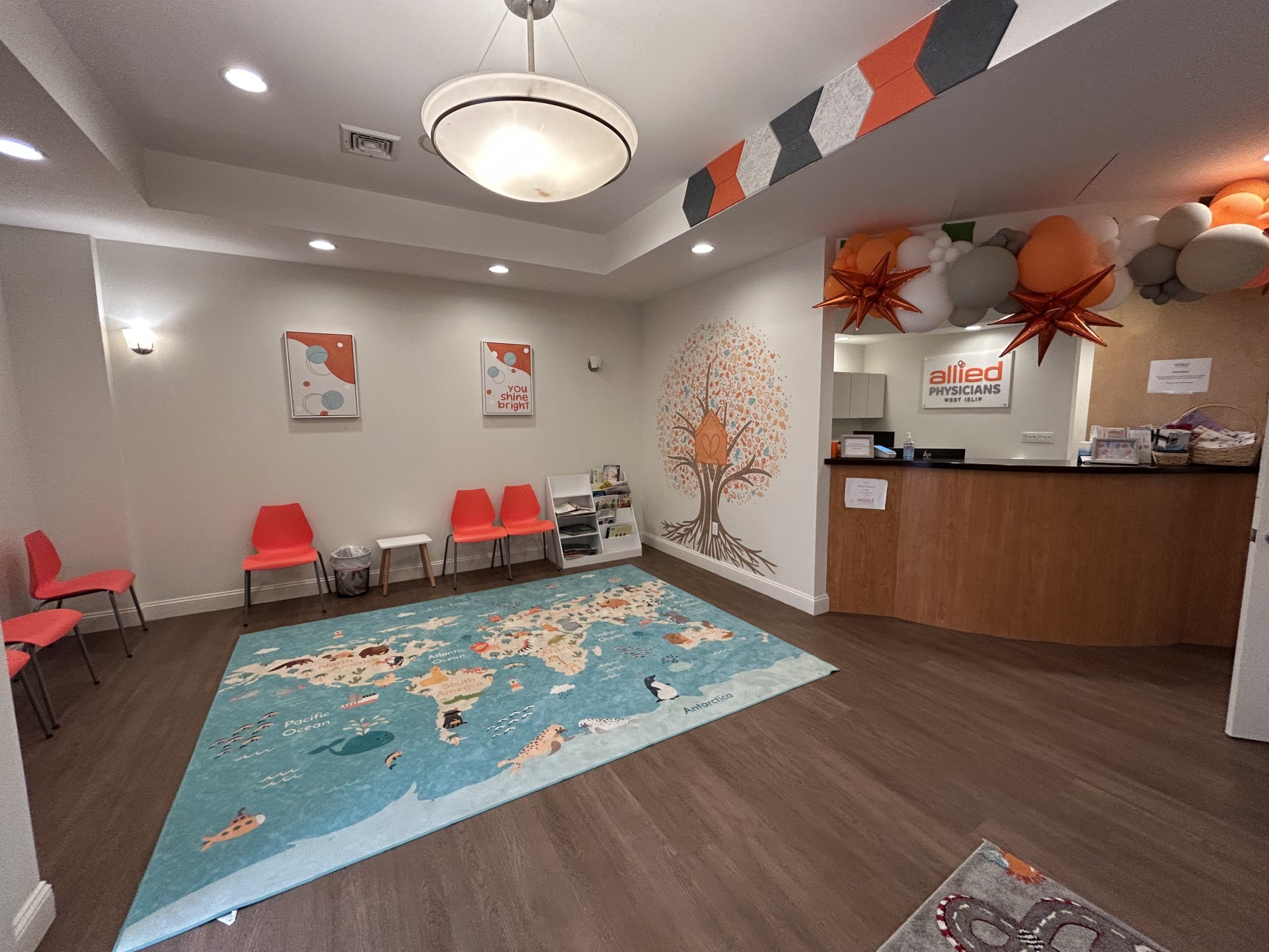 Waiting room of Allied Physicians with a world map rug, children’s chairs, and a front reception desk decorated with balloons.