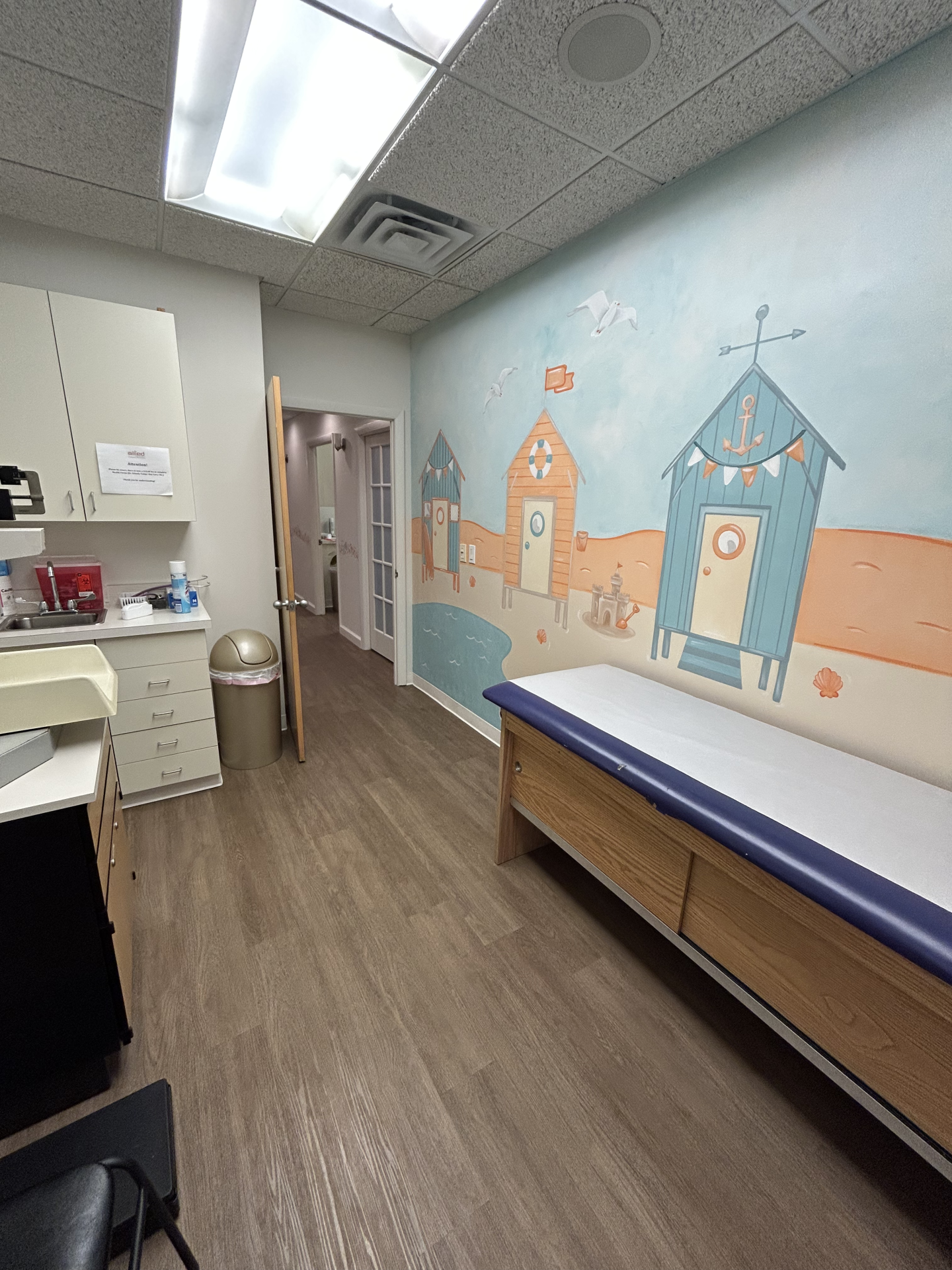 Medical exam room featuring a wall mural of beach huts and a blue-topped exam table.