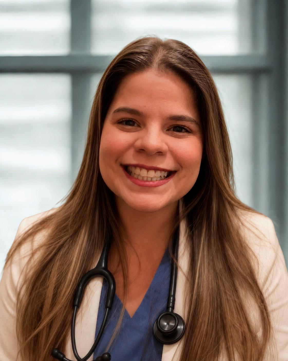 A woman with long brown hair, dressed in a white coat and blue top with a stethoscope around her neck, smiles at the camera. A blurred window is visible in the background.