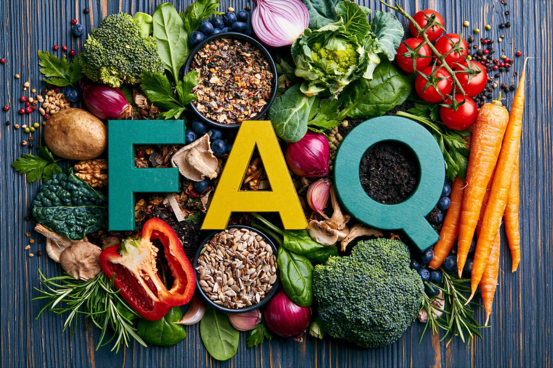 The letters FAQ made of wood sitting among a variety of fresh vegetables, berries, nuts, and seeds.